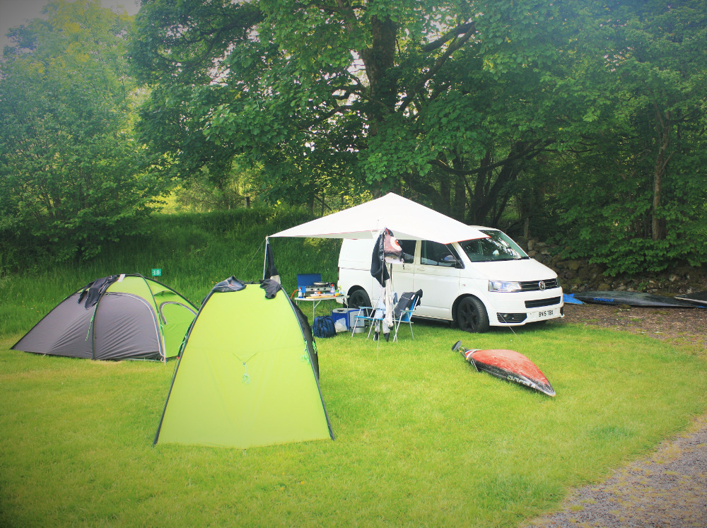 Tents, slalom kayaks and a VW van on a grass electric hook up pitch at Tyn Cornel