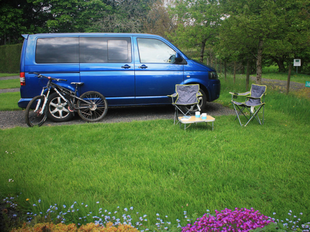 VW campervan and a mountain bike on a hardstanding touring pitch with a grassy area for picnics at Tyn Cornel Camping